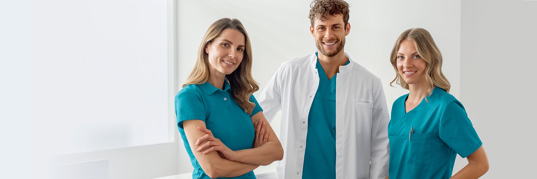 Un homme en blouse de médecin et en casaque turquoise et deux femmes en polo et en casaque turquoise dans un cabinet médical